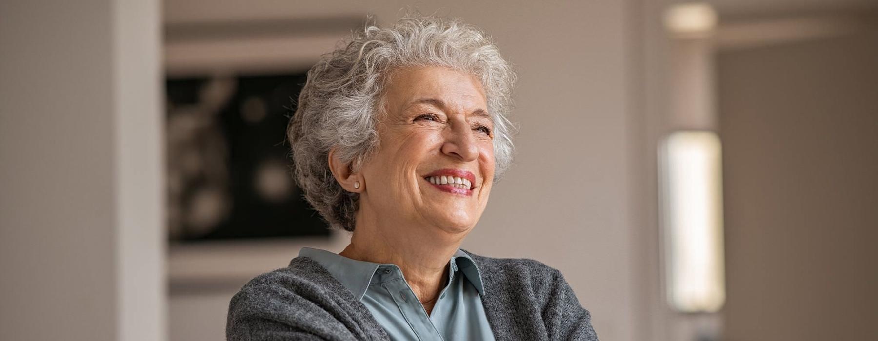 elderly woman with a cane, sits in a room and smiles